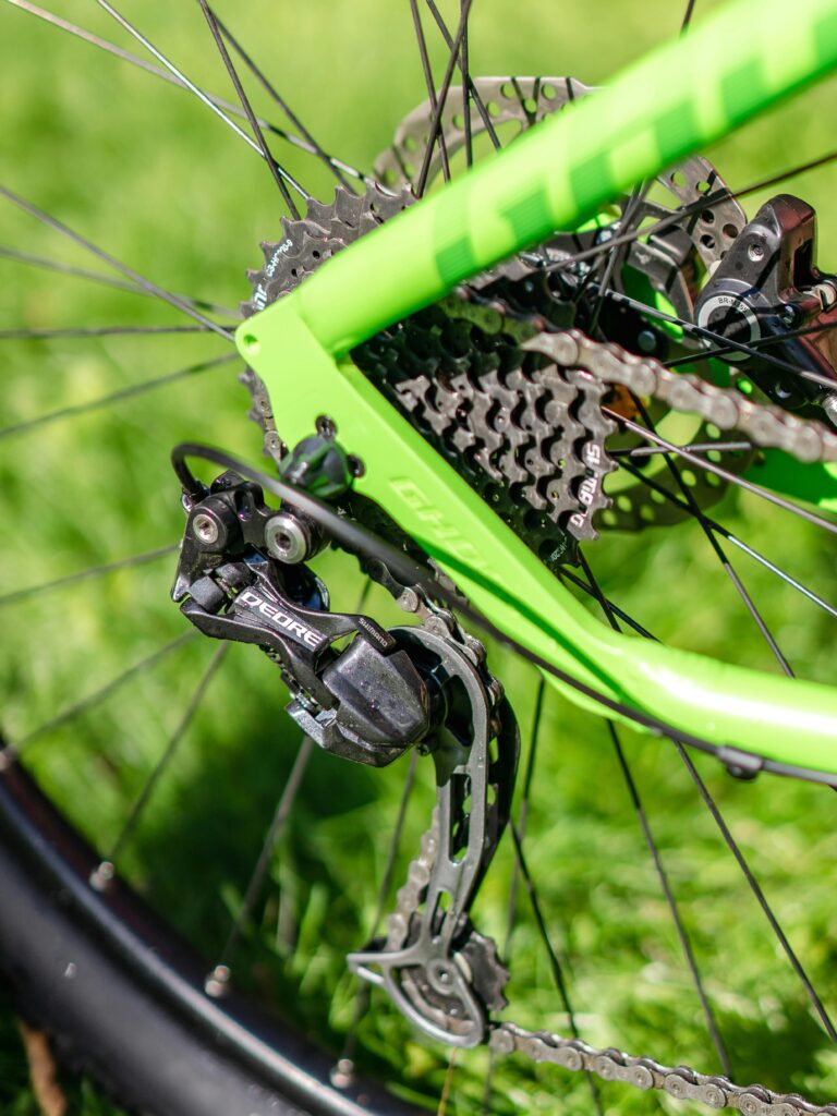 Detailed shot of a green bicycle gear and chain outdoors with a grassy background.